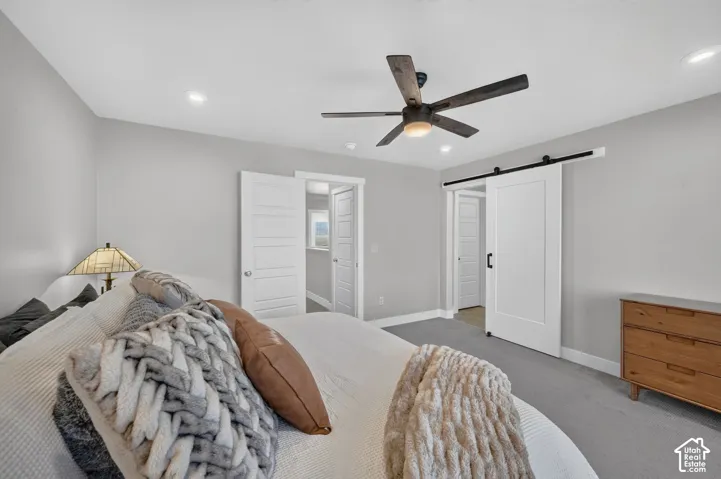 Recessed lighting, ceiling fan with integrated light, gray wall finishes, gray carpeting, and a white barn door on a black track