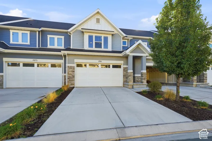 Multi-story exterior with blue siding, a peaked roofline, stone facade accents, an integrated garage with transom windows, and a paved driveway