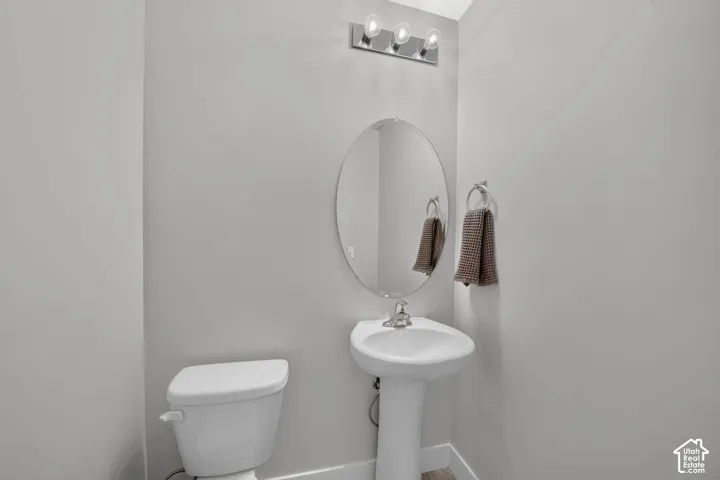Pedestal sink with chrome faucet, oval mirror, and three-bulb vanity light fixture