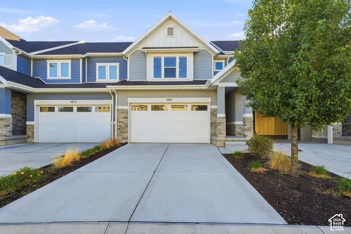 Contemporary facade with stone accents, covered entry, attached garage, and concrete driveway