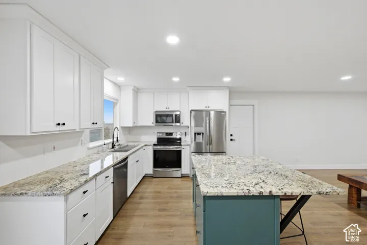 Kitchen featuring white cabinetry, stainless steel appliances, speckled stone countertops, a central island with a contrasting base, and wood-finish flooring