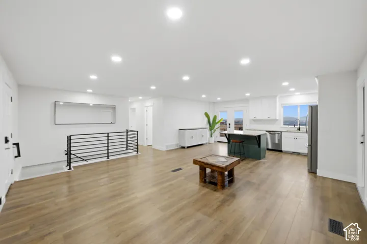 Expansive open-concept space featuring wood-finish flooring, recessed lighting, and a modern black metal railing