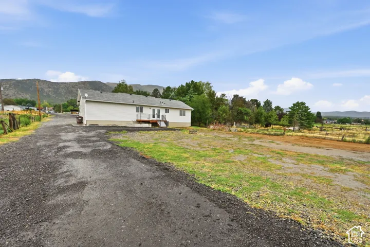 White siding exterior with a pitched roof, rear deck with railings, double glass doors, and a gravel driveway