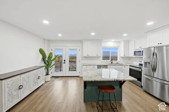 Kitchen featuring white shaker cabinetry, stainless steel appliances, a center island with granite countertop, and wood-finish flooring