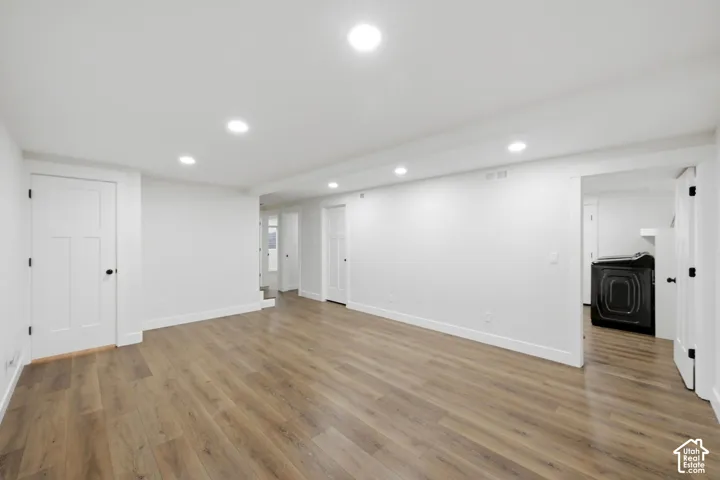 Recessed lighting, wood-finish flooring, white walls, white paneled doors, and a built-in black washing machine
