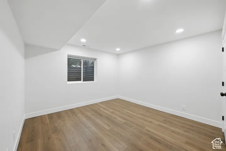 Recessed lighting, wood-finish flooring, white walls, white trim, and a window with horizontal blinds