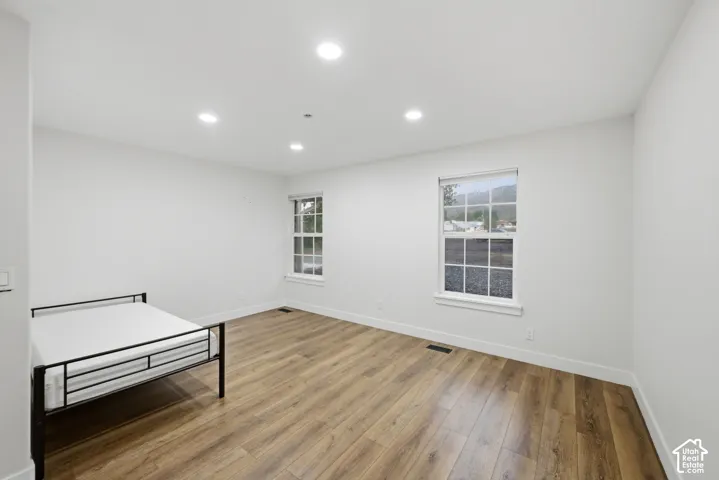 Recessed lighting, wood-finish flooring, white trim, dual windows, and clean white walls