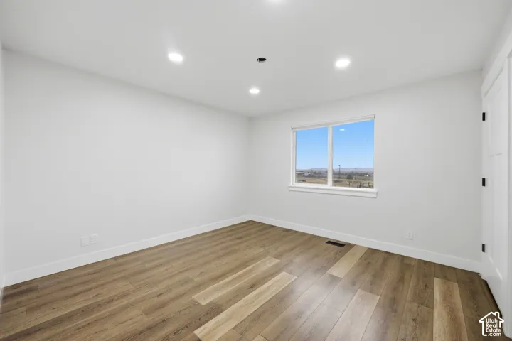 Wood-finish flooring with white walls, recessed ceiling lighting, and a window framing the exterior scenery