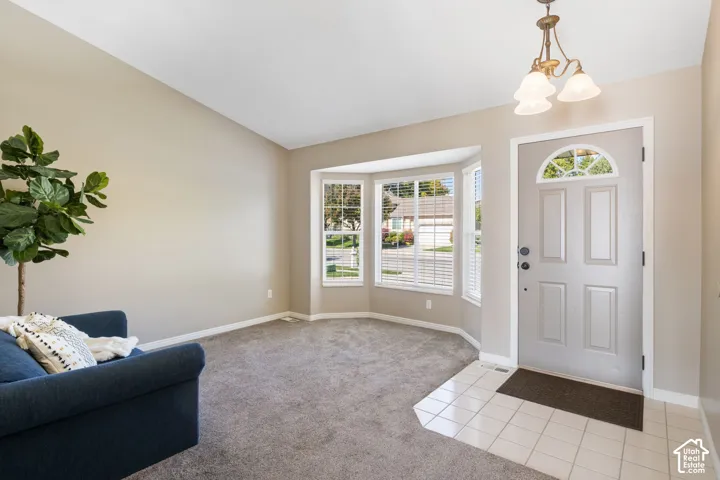 Vaulted ceiling, paneled entry door with transom window, bay window with blinds, carpeted flooring, and tiled entryway