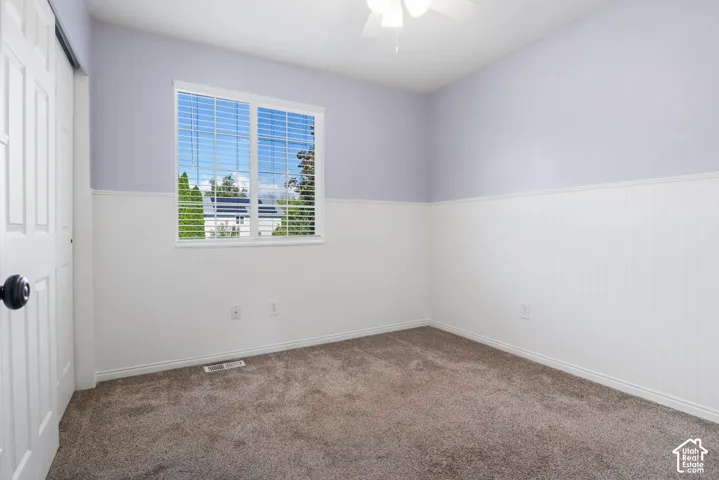 Light-filled room featuring a dual window, wainscoting, textured carpet, and ceiling fan