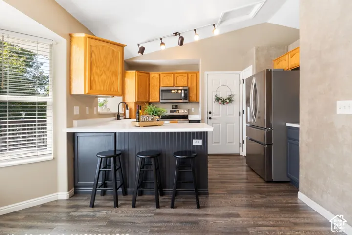 Wood-finish flooring, white countertop with breakfast bar, stainless steel appliances, track lighting, and a white paneled door