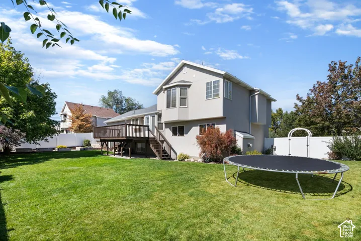 Expansive backyard featuring a manicured lawn, mature trees, and a multi-level deck with stairs