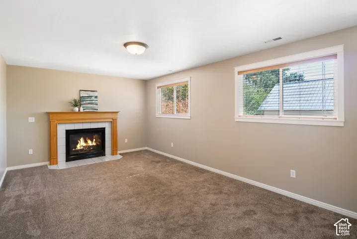 Carpeted interior space with a fireplace featuring a light wood mantel and white tile surround