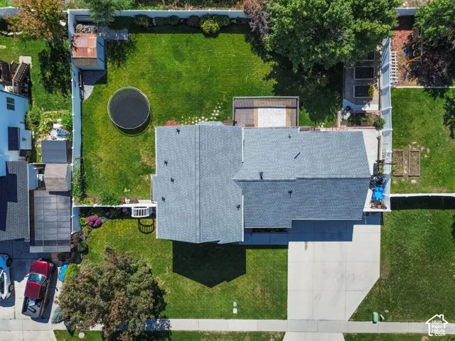 Expansive green lawn with a large concrete driveway, a wooden deck, a storage shed, and raised garden beds