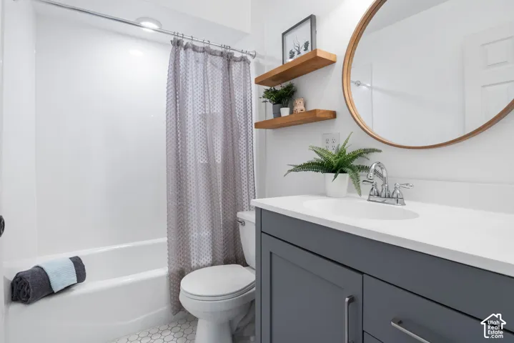 White bathtub and shower combination with chrome fixtures, a dark gray vanity with a single basin sink, a round mirror, and hexagonal floor tiling