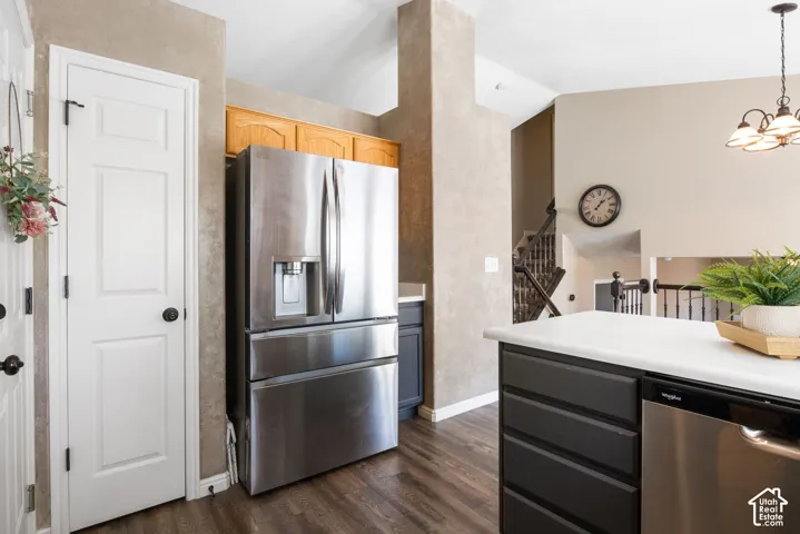 Stainless steel French door refrigerator, wood-finish flooring, dark cabinetry, light-toned countertops, and an integrated stainless steel dishwasher