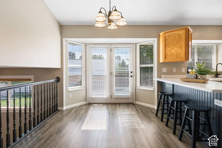 Wood-finish flooring, bay window with French doors, contemporary chandelier, breakfast bar with beadboard paneling, and oak-finish cabinetry
