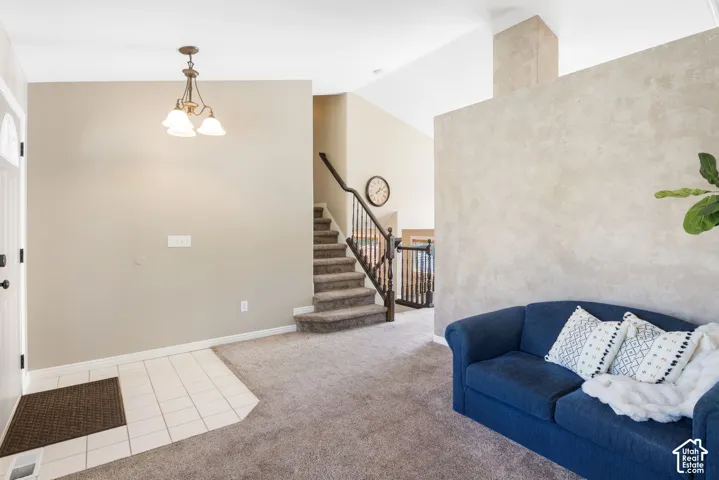 Entryway featuring tiled flooring, a decorative chandelier, and a carpeted staircase with a dark wood handrail and balusters