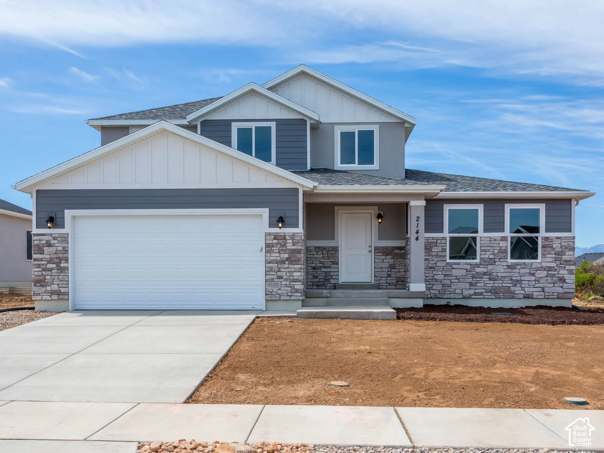 Two-story residence featuring a covered entry, stone and siding exterior, concrete driveway, and attached garage