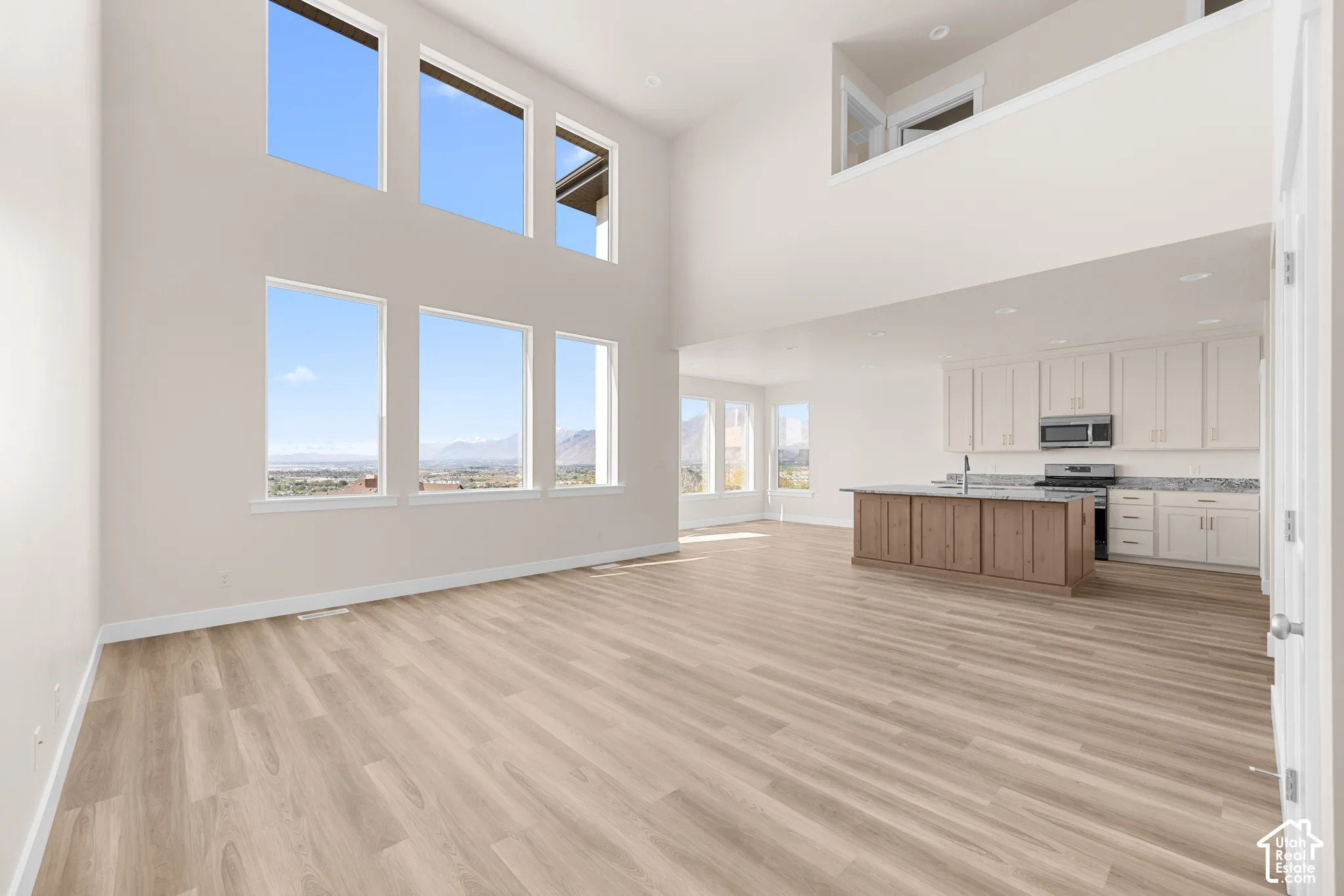 Soaring ceilings, abundant natural light, wood-finish flooring, a kitchen island with a sink, and stainless steel appliances
