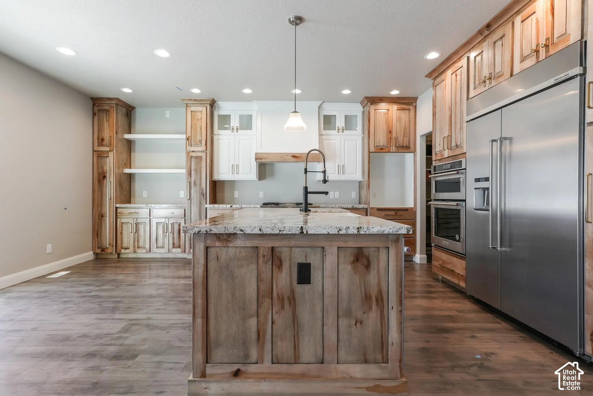 Kitchen featuring wood-finish flooring, a central island with a stone countertop, a built-in double oven, and a stainless steel refrigerator