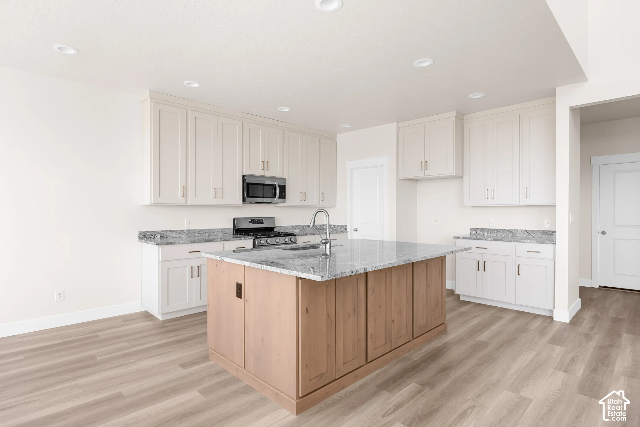 Kitchen featuring light wood-finish flooring, white cabinetry, a central island with natural wood-finish paneling, stainless steel appliances, and recessed lighting