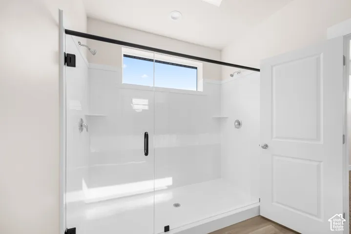 Spacious shower enclosure with clear glass doors, white paneling, integrated shelving, and a transom window
