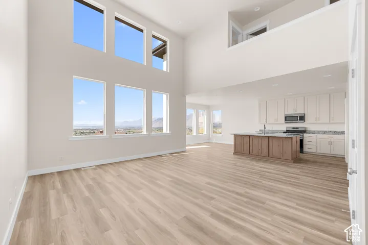 Soaring ceilings, abundant natural light, wood-finish flooring, a kitchen island with a sink, and stainless steel appliances