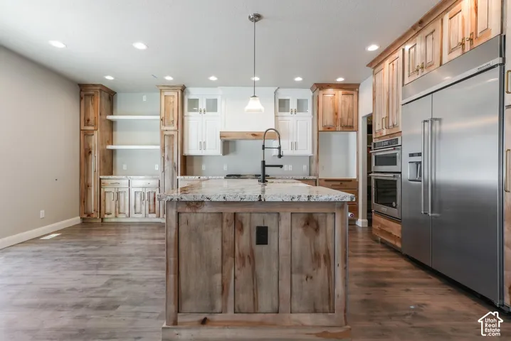 Kitchen featuring wood-finish flooring, a central island with a stone countertop, a built-in double oven, and a stainless steel refrigerator