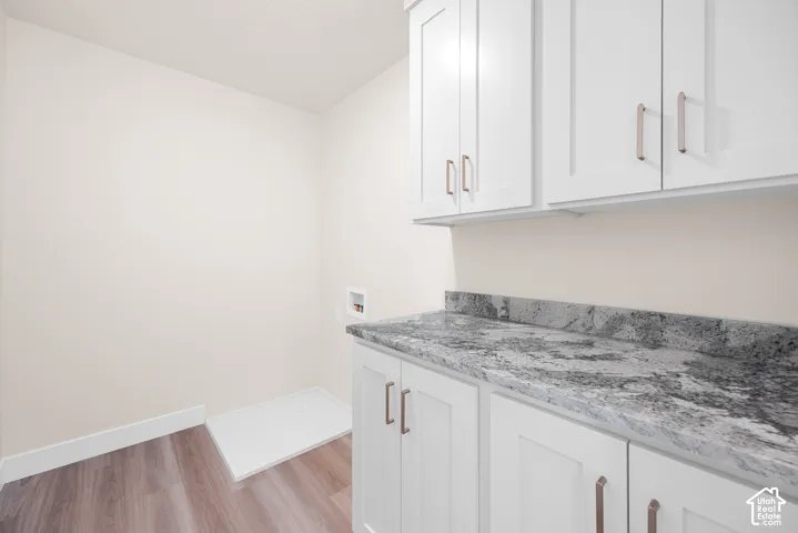 Laundry area with wood-finish flooring, white shaker cabinetry, and a patterned countertop