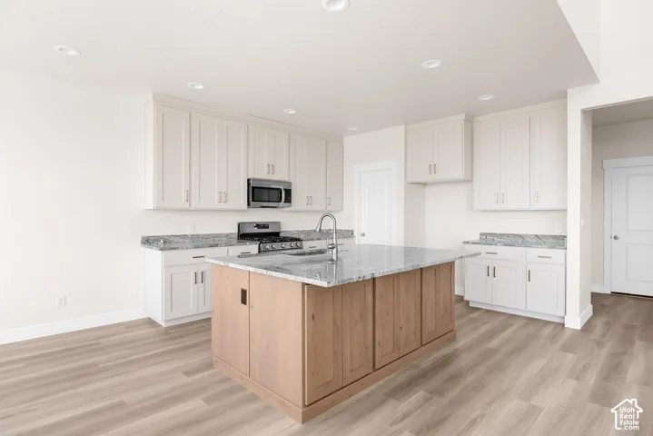 Kitchen featuring light wood-finish flooring, white cabinetry, a central island with natural wood-finish paneling, stainless steel appliances, and recessed lighting