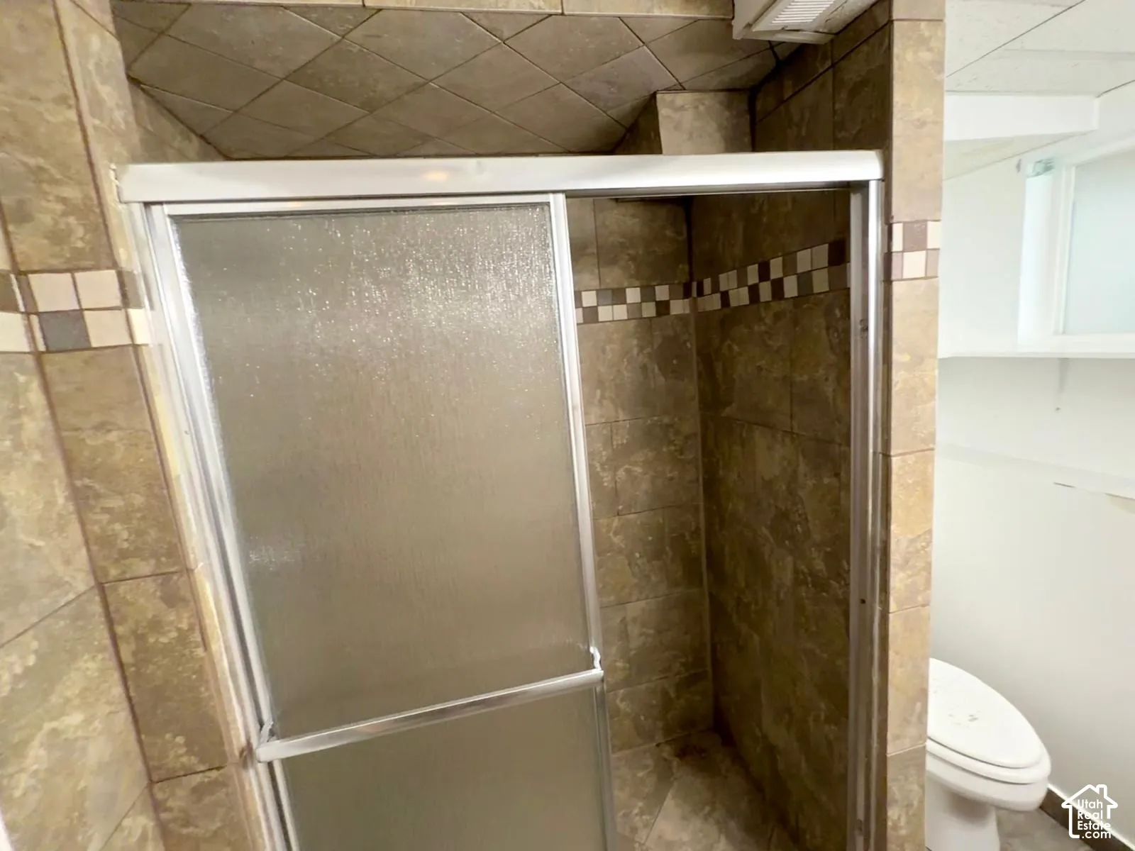 Tiled shower stall with sliding glass doors, accented by a decorative tile band