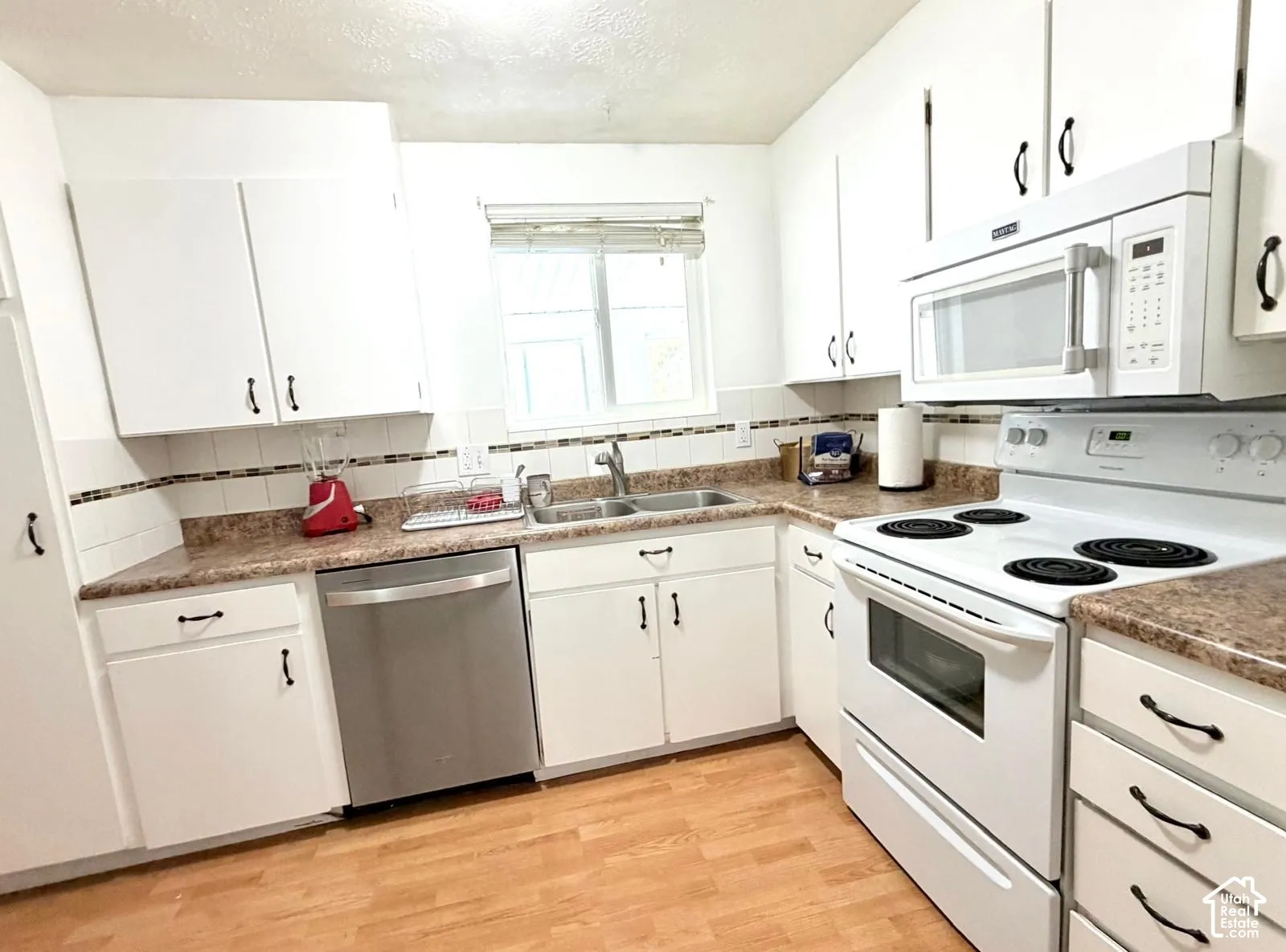 White cabinetry, stainless steel dishwasher, over-range microwave, wood-finish flooring, and a double basin sink