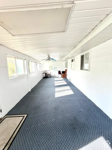 Spacious enclosed porch with continuous windows, blue patterned carpeting, white paneled ceiling, and a ceiling fan