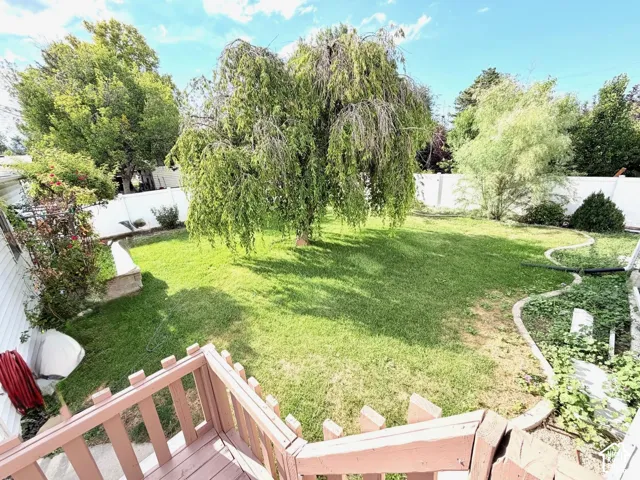Expansive backyard featuring a manicured lawn, established trees, and white privacy fencing