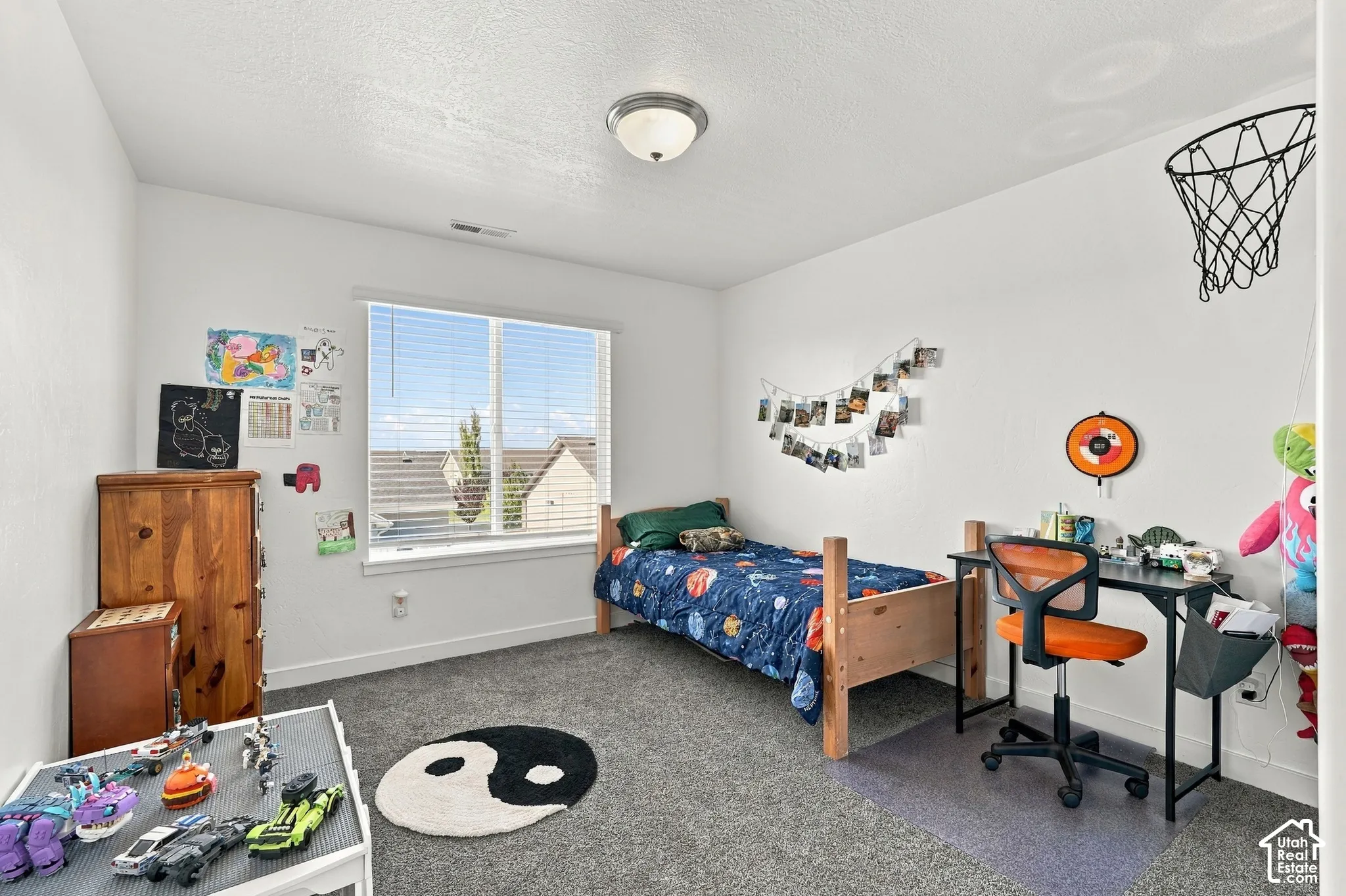 Carpeted room featuring a large window with blinds, ceiling-mounted lighting, and neutral wall tones