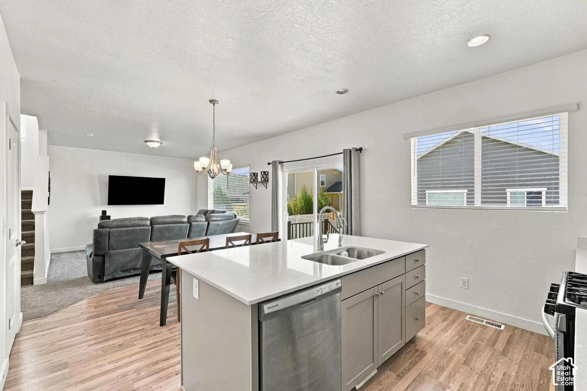 Open-concept living area featuring wood-finish flooring, a kitchen island with dual sinks, and a sliding glass door leading to the exterior