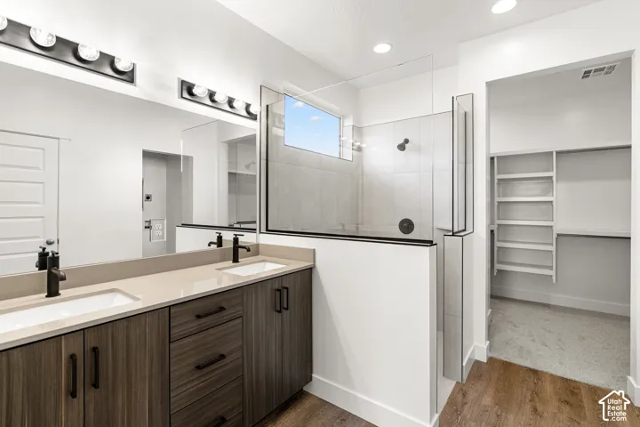 Dual vanity with integrated sinks, wood-finish cabinetry, matte black fixtures, and a glass-enclosed shower with tiled walls and a transom window