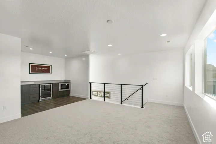 Carpeted living area with recessed lighting, multiple windows, and a black metal railing
