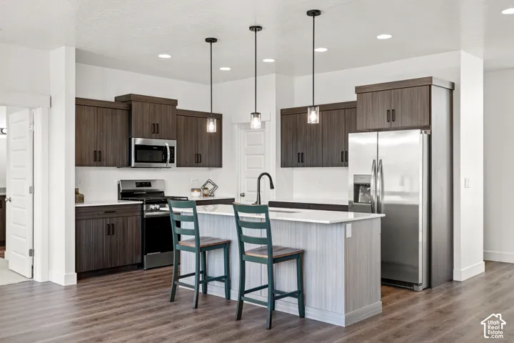 Kitchen featuring stainless steel appliances, dark wood-finish cabinetry, recessed lighting, and a kitchen island with pendant lighting