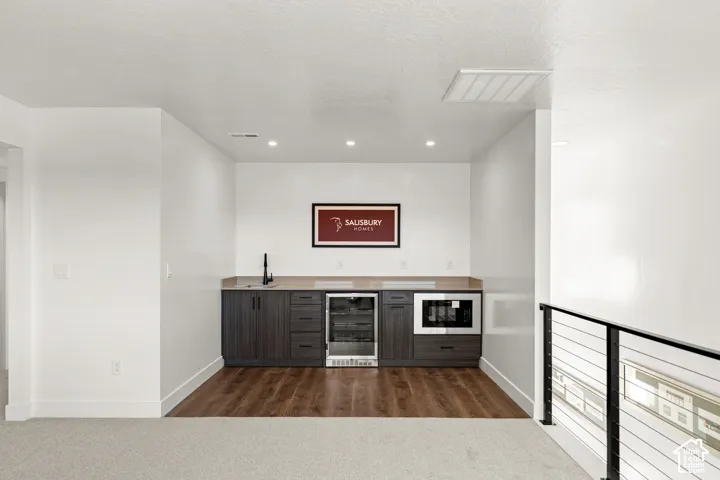 Built-in wet bar featuring a beverage cooler, microwave, dark wood-finish cabinetry, and a countertop with an undermount sink