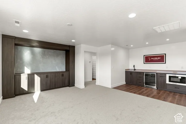 Built-in media center cabinetry, recessed lighting, wet bar with under-counter beverage refrigerator, microwave, and wood-finish flooring