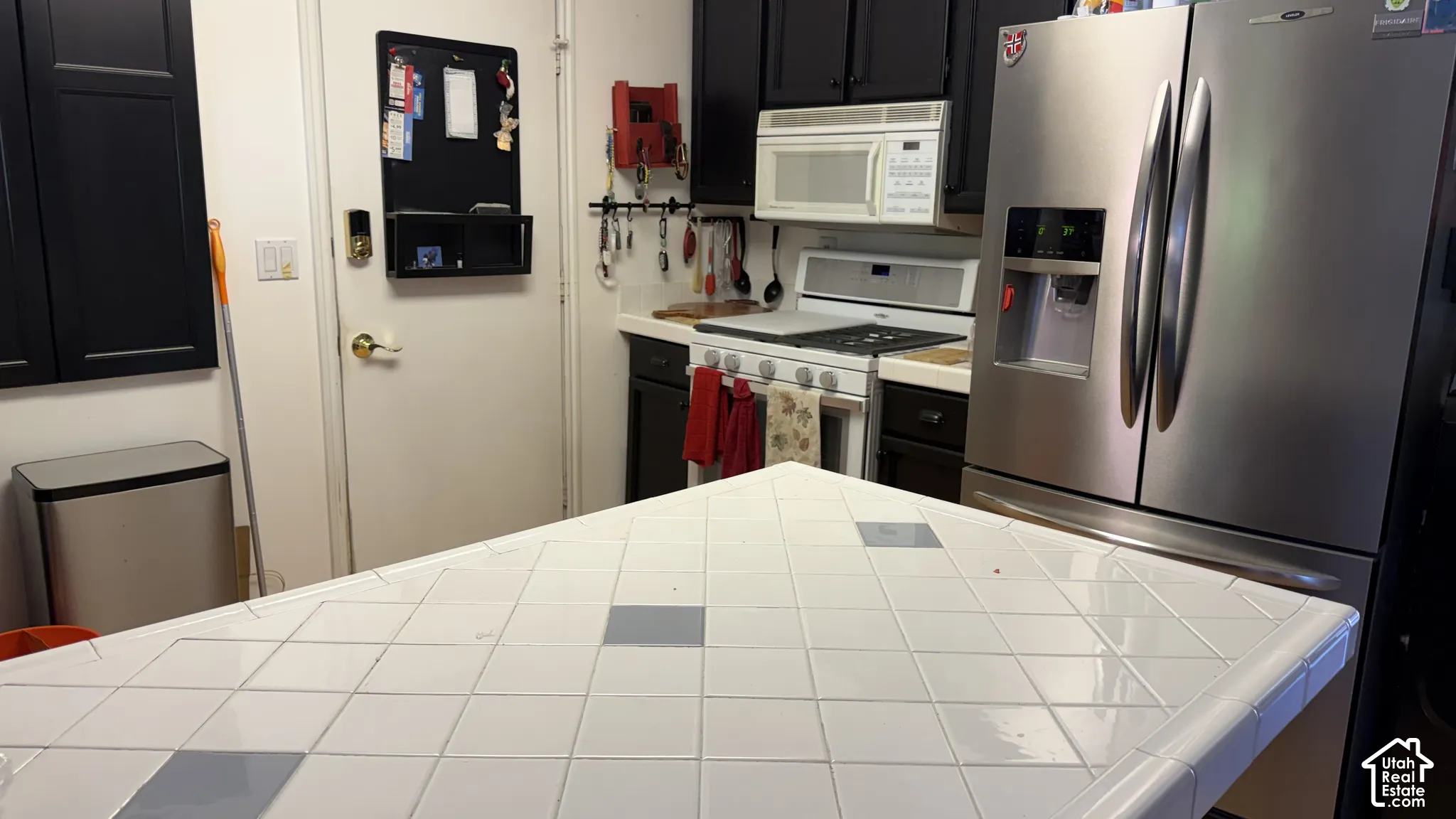 Kitchen featuring a tile countertop, white gas range, stainless steel refrigerator, white microwave, and dark cabinetry