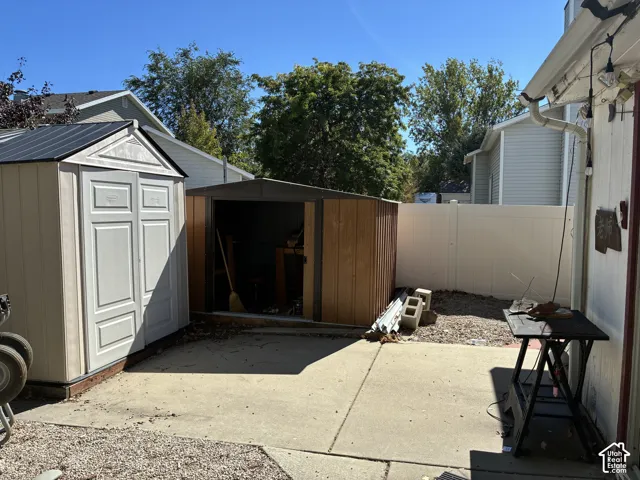 Concrete patio with two storage sheds and a white privacy fence