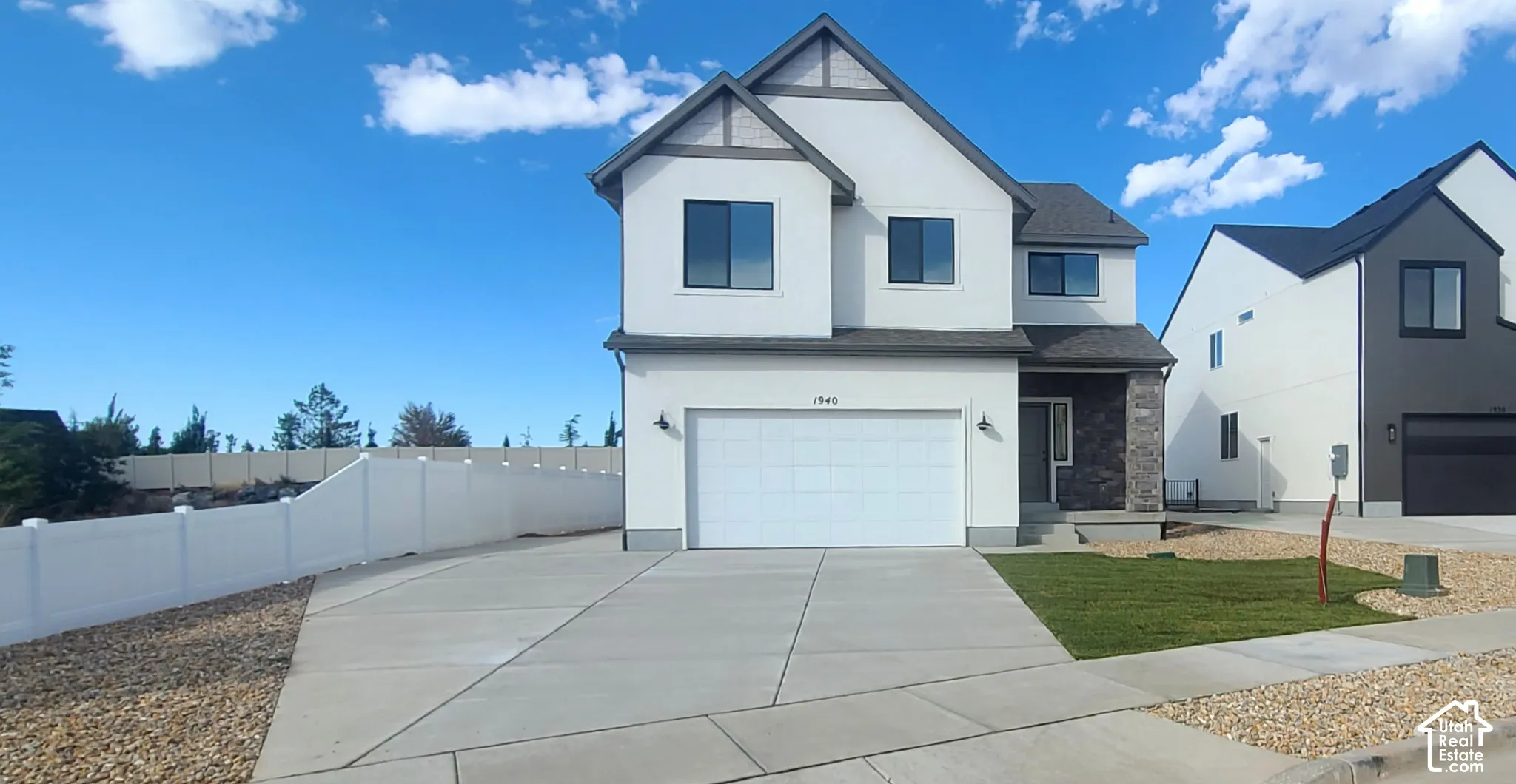 Two-story residence featuring a combination of smooth stucco and stone veneer siding, a concrete driveway, a white vinyl privacy fence, and a two-car garage