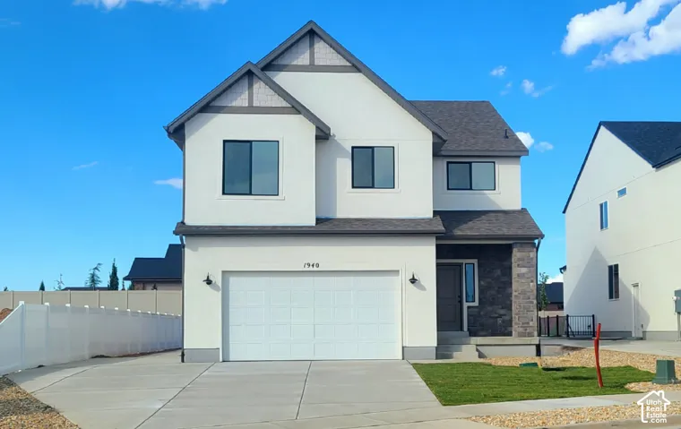 Two-story exterior featuring a light-toned stucco finish, partial stone veneer facade, asphalt shingle roofing, and an attached two-car garage