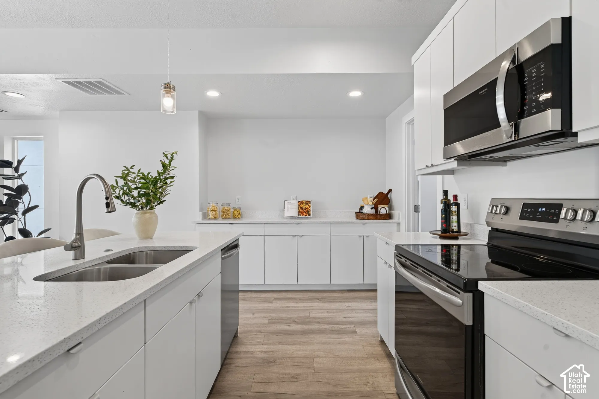 Kitchen featuring white cabinetry, light-toned countertops, stainless steel appliances, and wood-finish flooring