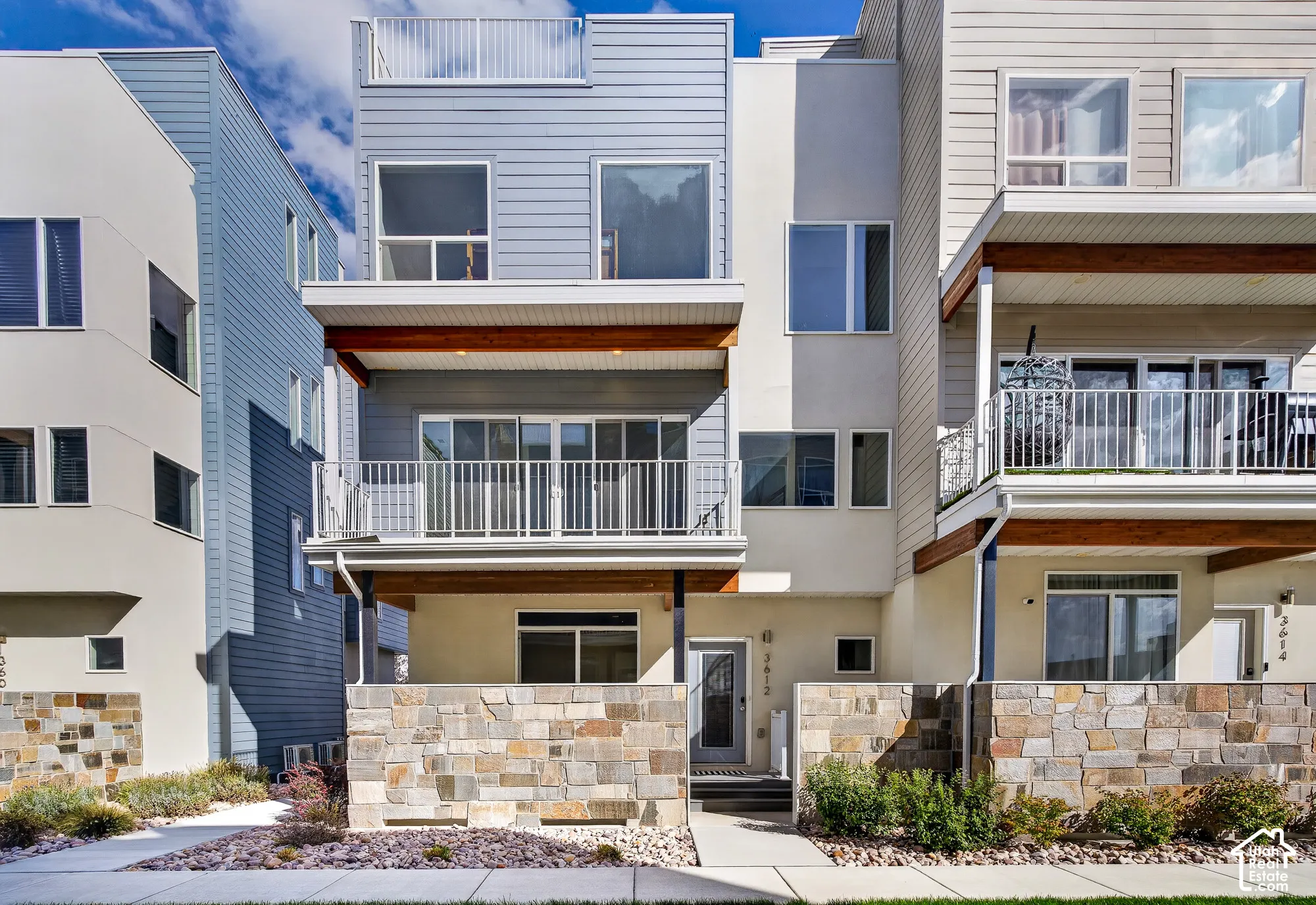 Contemporary facade with stone wall accents, multiple balconies, a rooftop deck, and a mix of siding and stucco finishes