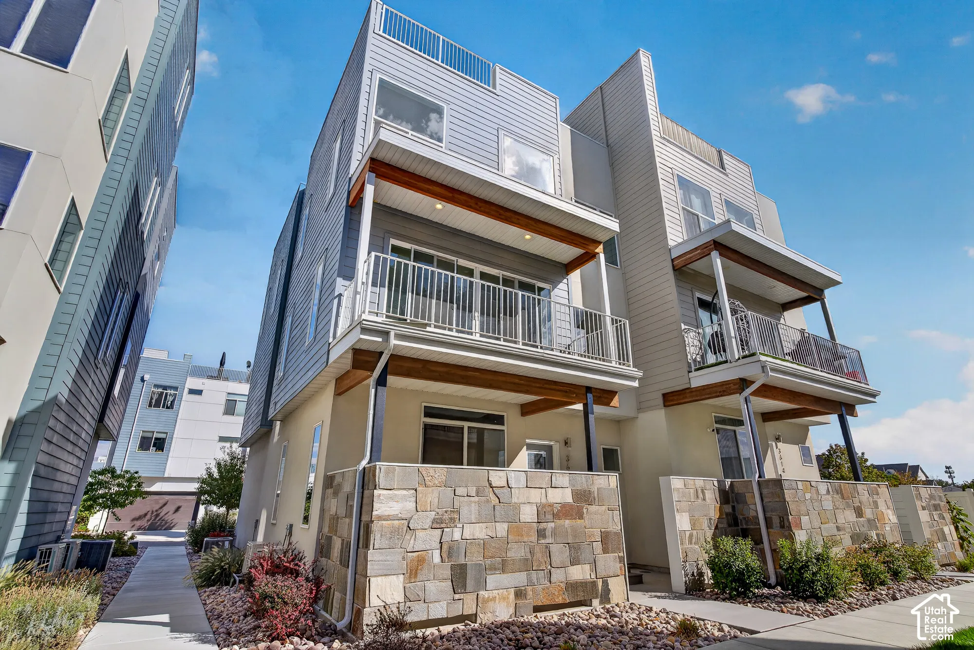 Contemporary multi-level exterior with stone veneer accents, multiple balconies with metal railings, and horizontal siding