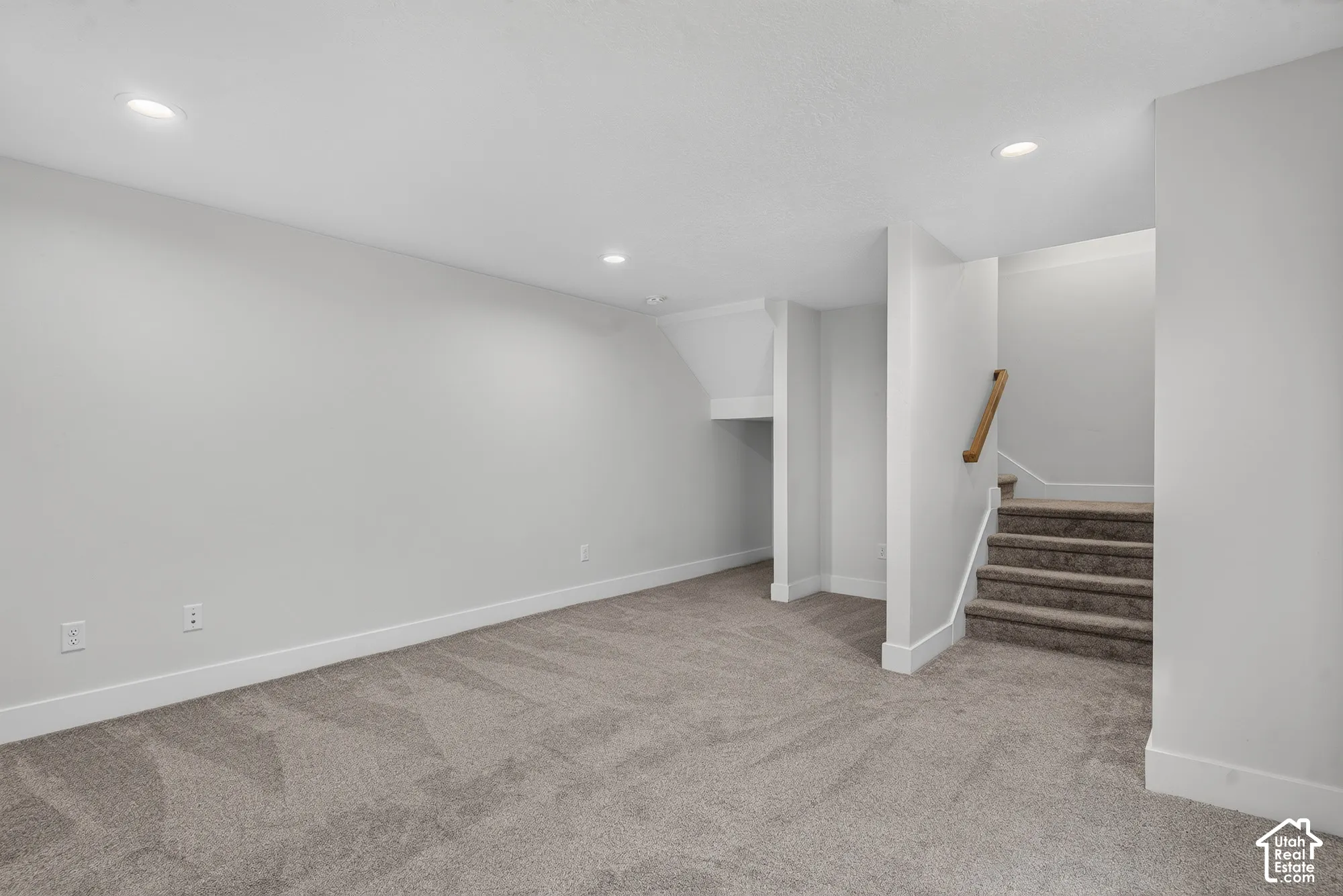 Recessed lighting, light gray carpeting, white walls, white baseboards, and a wooden handrail